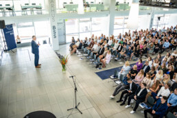 Oversigtsbillede af fyldt auditorium ved Aarhus BSS, hvor en taler engagerer publikum under en ceremoni. Foto af Kasper Hornbæk.